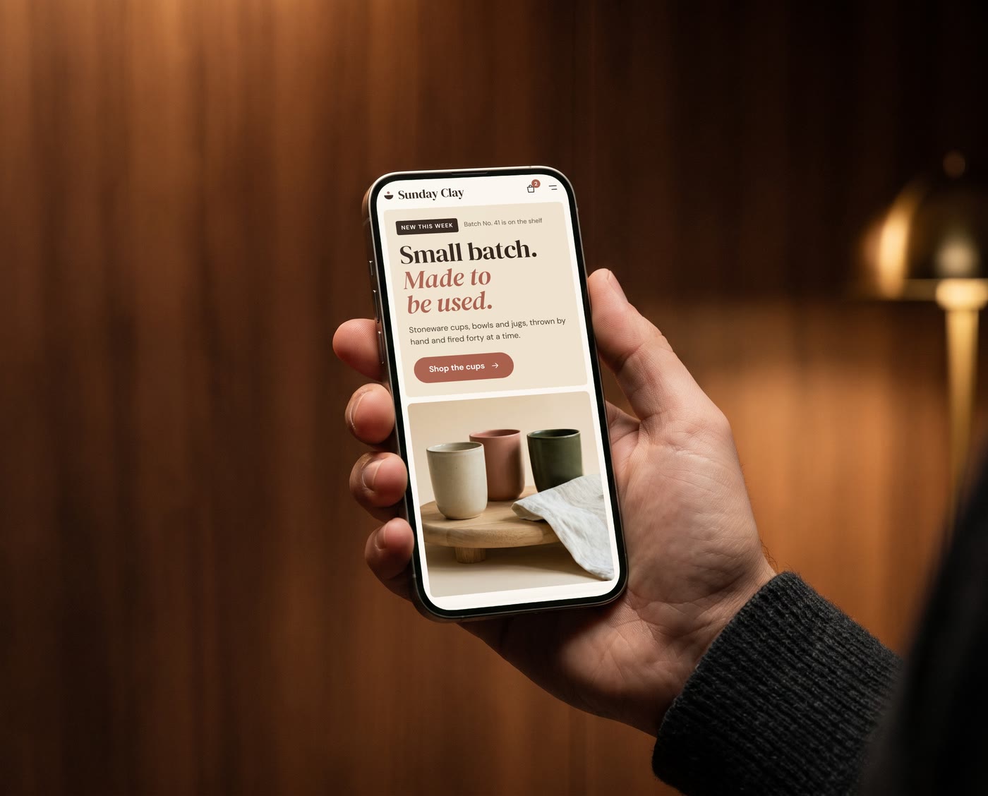 A hand holding a phone that shows one of the websites, in a warm, dimly lit office.